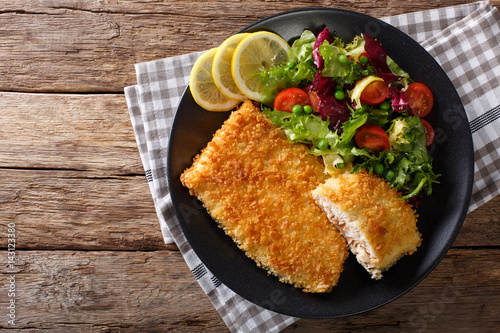 Fried Arctic char fish fillet in breadcrumbs and fresh vegetable salad close-up. horizontal top view