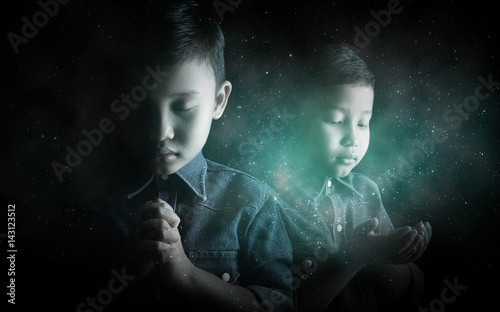 Little boy praying and praising God with stardust background.