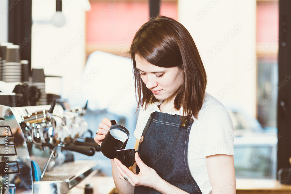 young female barista adding milk to coffee and smiling while standing at the bar counter in the urban cafe young female barista adding milk to coffee and smiling while standing at the bar counter in the urban cafe
