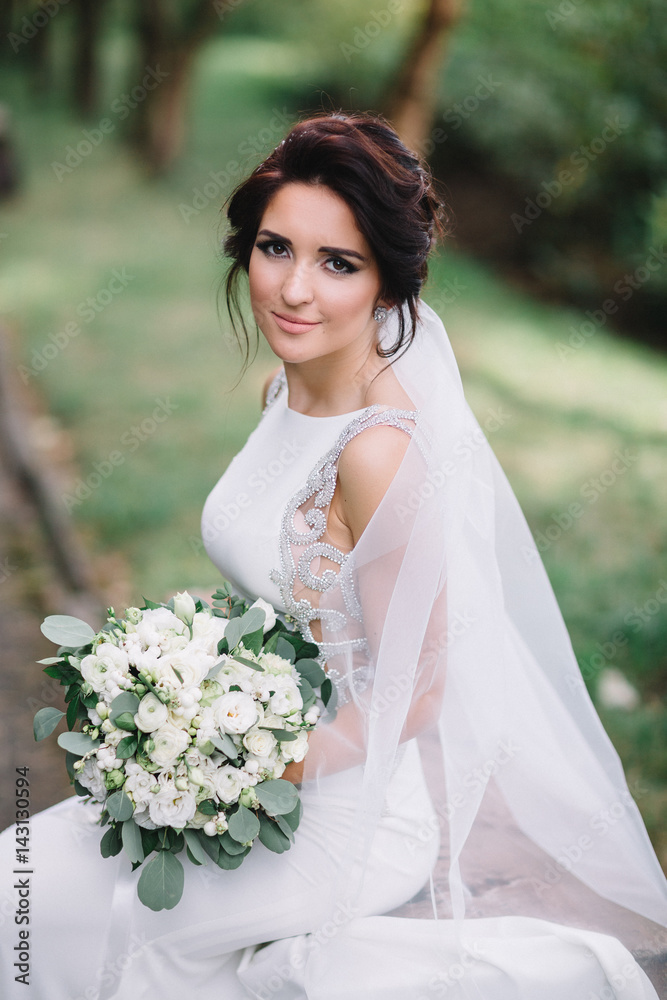 Bride in elegant wedding gown sits on stone bench