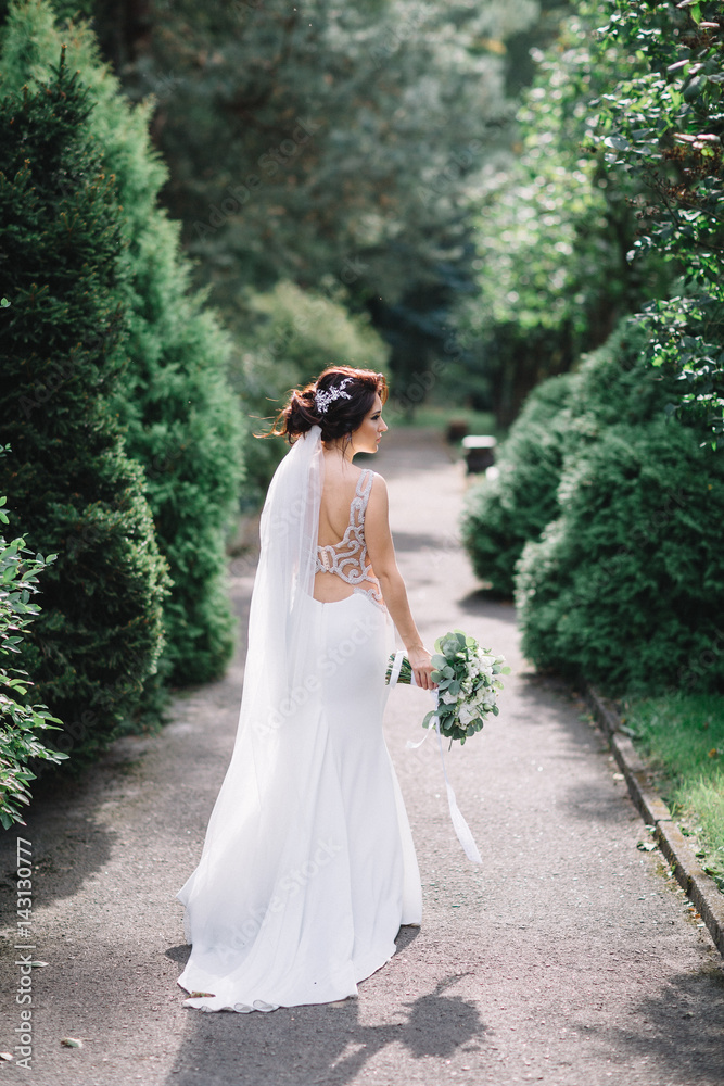 Bride in dress with crystalks walks along the path in green park Bride in dress with crystalks walks along the path in green park