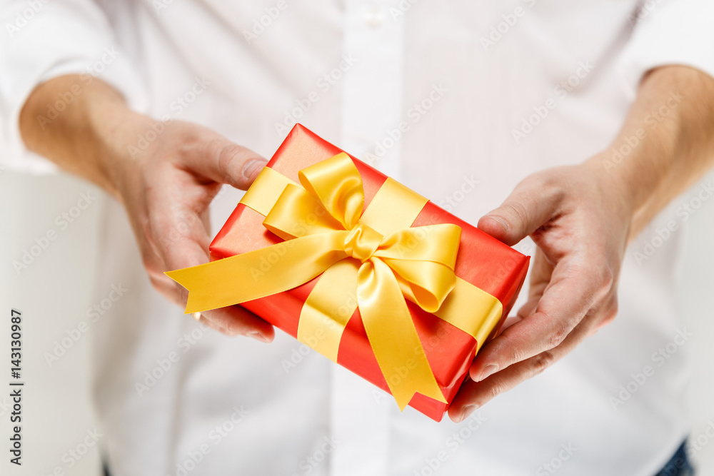 Male hands holding a gift box. Present wrapped with ribbon and bow. Christmas or birthday red package. Man in white shirt. Male hands holding a gift box. Present wrapped with ribbon and bow. Christmas or birthday red package. Man in white shirt.
