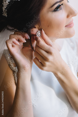 Bride puts on her ears earrings like crystal flowers