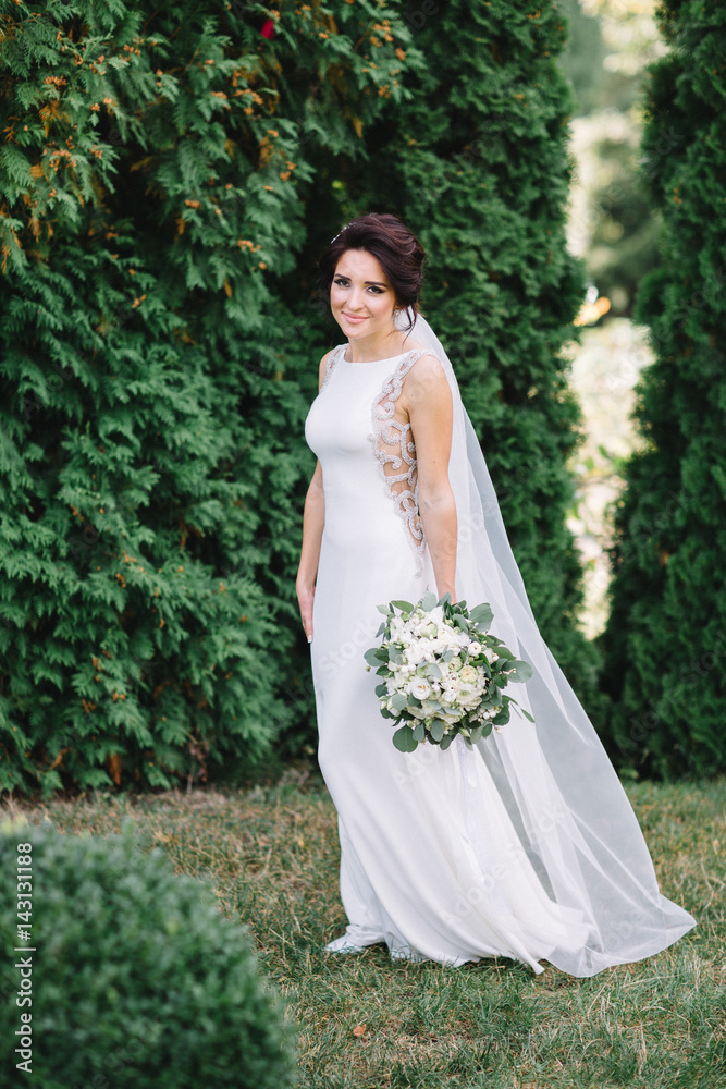 Stunning bride with deep dark eyes poses with wedding bouquet in the forest