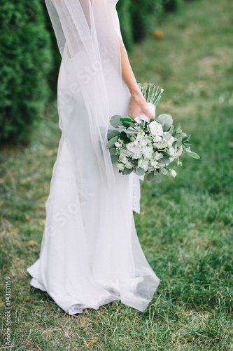 Gorgeous white wedding bouquet held by bride standing on green lawn