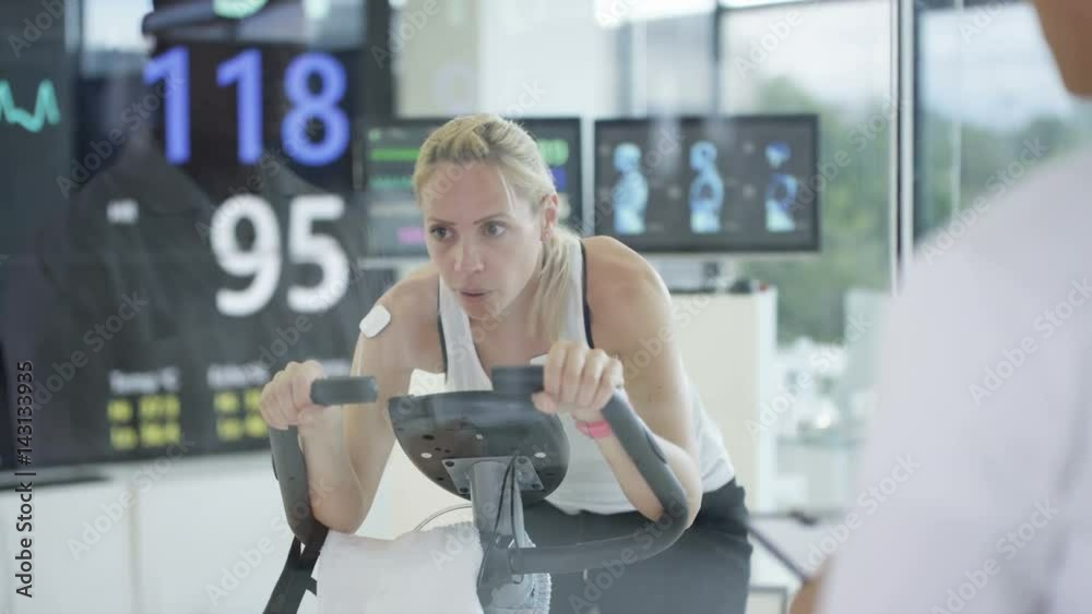 Female athlete on exercise bike being tested and monitored by sports scientist. Female athlete on exercise bike being tested and monitored by sports scientist.