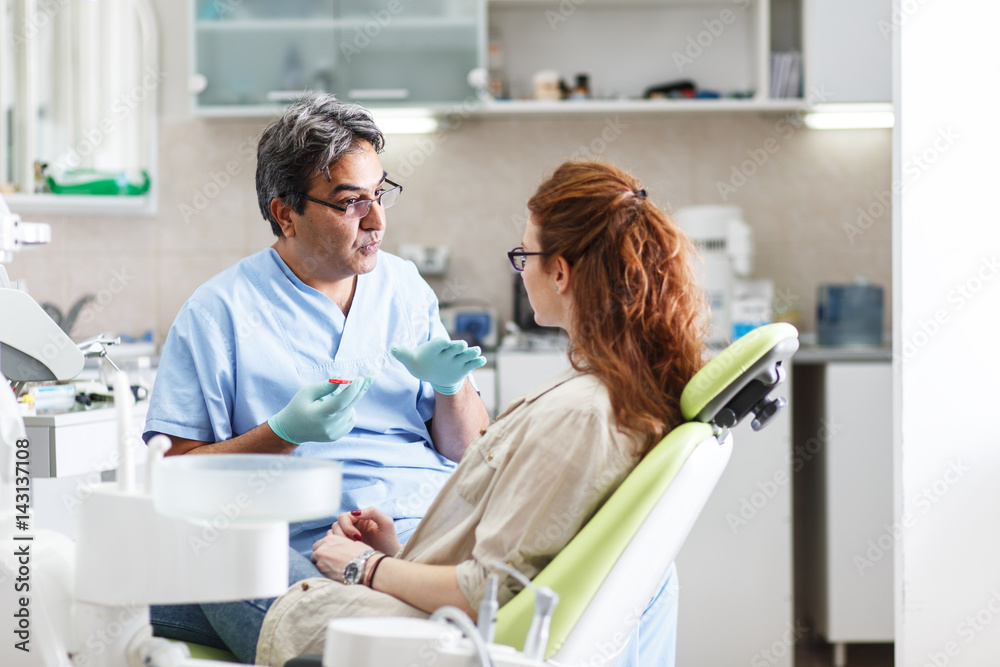 A professional dentist, equipped with a bright smile, converses with his red-haired female patient, carefully explaining the upcoming treatment, and ensuring her comfort throughout the process. A professional dentist, equipped with a bright smile, converses with his red-haired female patient, carefully explaining the upcoming treatment, and ensuring her comfort throughout the process.