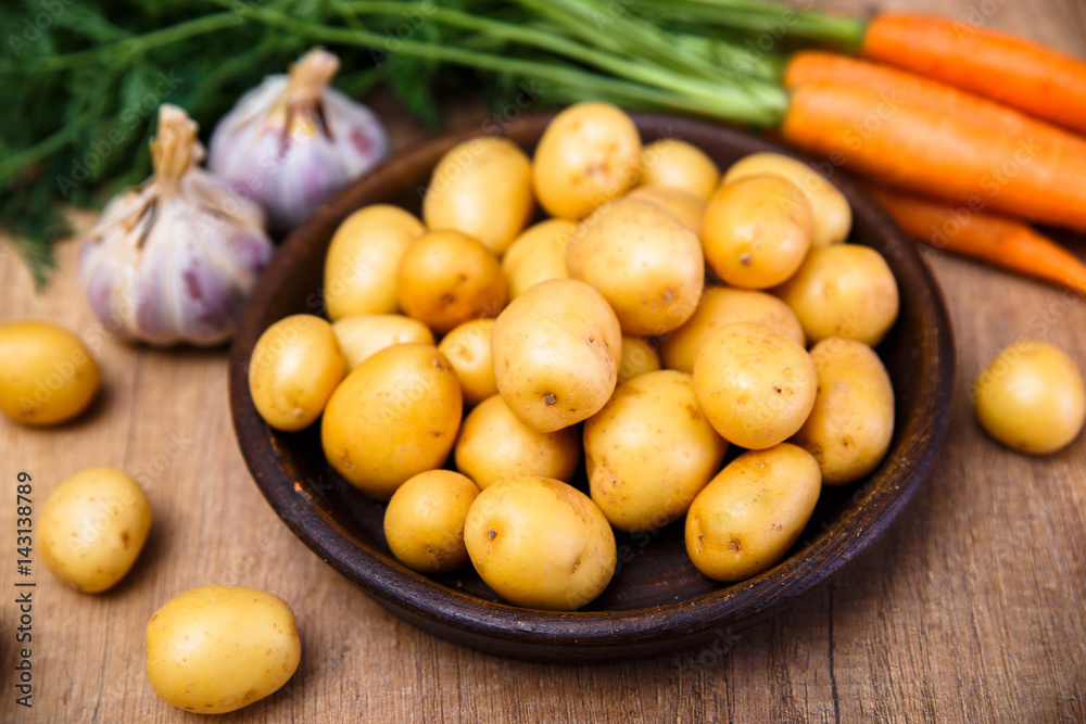 Potatoes in plate. Carrot, garlic and raw new potato. Fresh natural vegetables. Organic bio food on rustic wooden table.