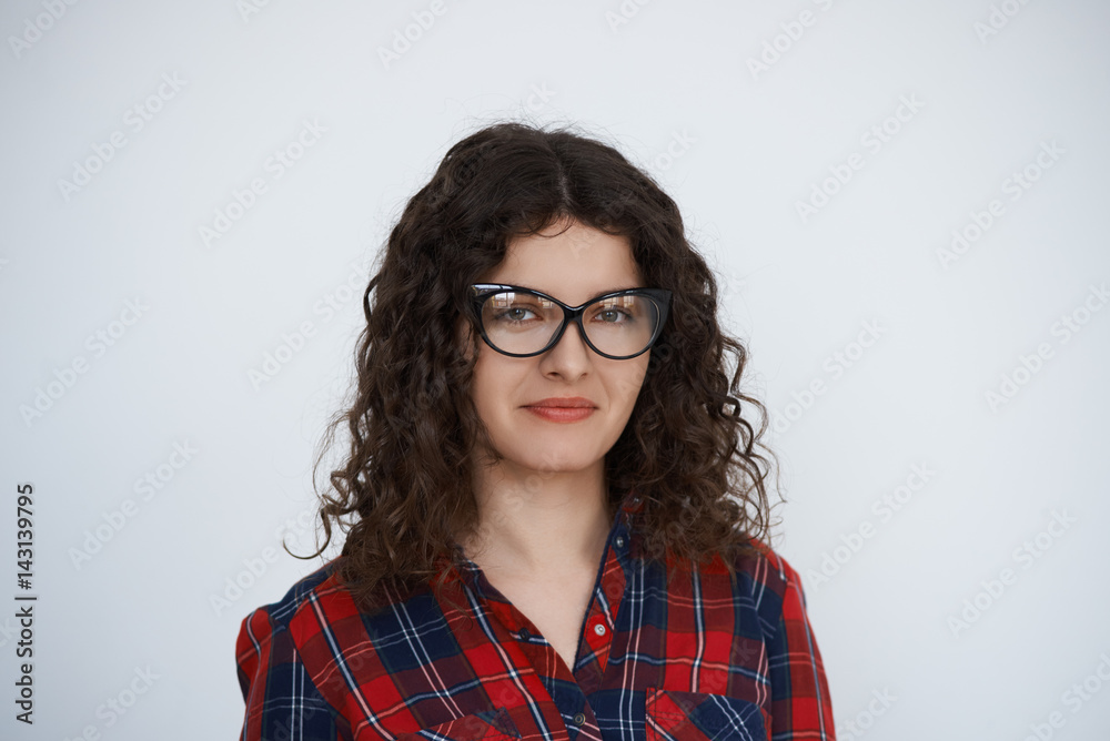 Young attractive smiling Curly hair programmer woman in trendy glasses dressed in check shirt look to the camera. Talented manager with long hair portrait on neutral background feel good.