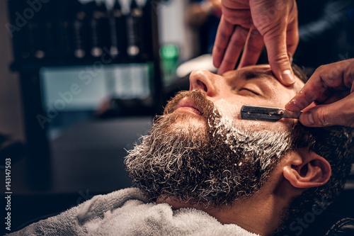 Close up image of barber shaving a man with a sharp steel razor. photo
