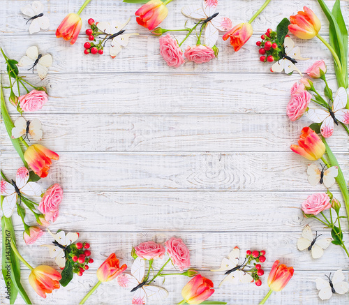 Floral frame with spring flowers and butterflies over wooden background