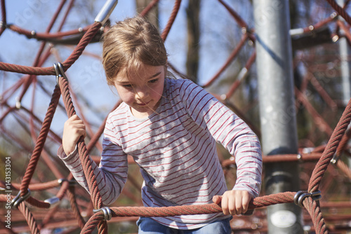Active young child girl climbing the spider web playground activity. Children summer activities.