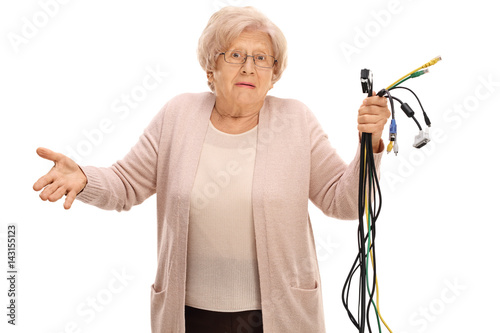 Photos Confused elderly woman holding different types of electronic cables