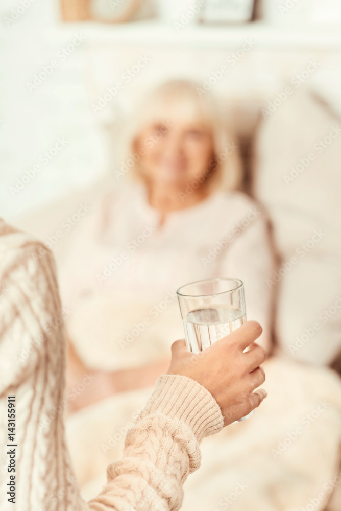 Positive woman giving glass of water for ill mother Positive woman giving glass of water for ill mother