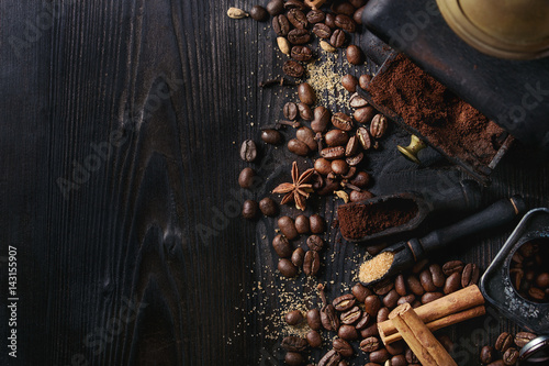 Black roasted coffee beans and grind with spices cinnamon, anise, cardamom, clove and brown sugar. With black vintage coffee grinder and scoops over wood burnt background. Top view