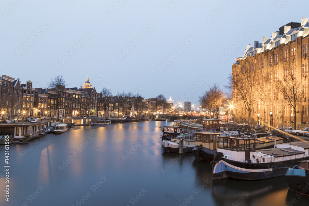 Naklejka premium Amsterdam, March 17, 2017: Canals and house view from Amsterdam, during the twilight where city of bikes, canals and peace