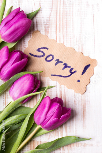 word SORRY and bouquet of tulips on wooden background