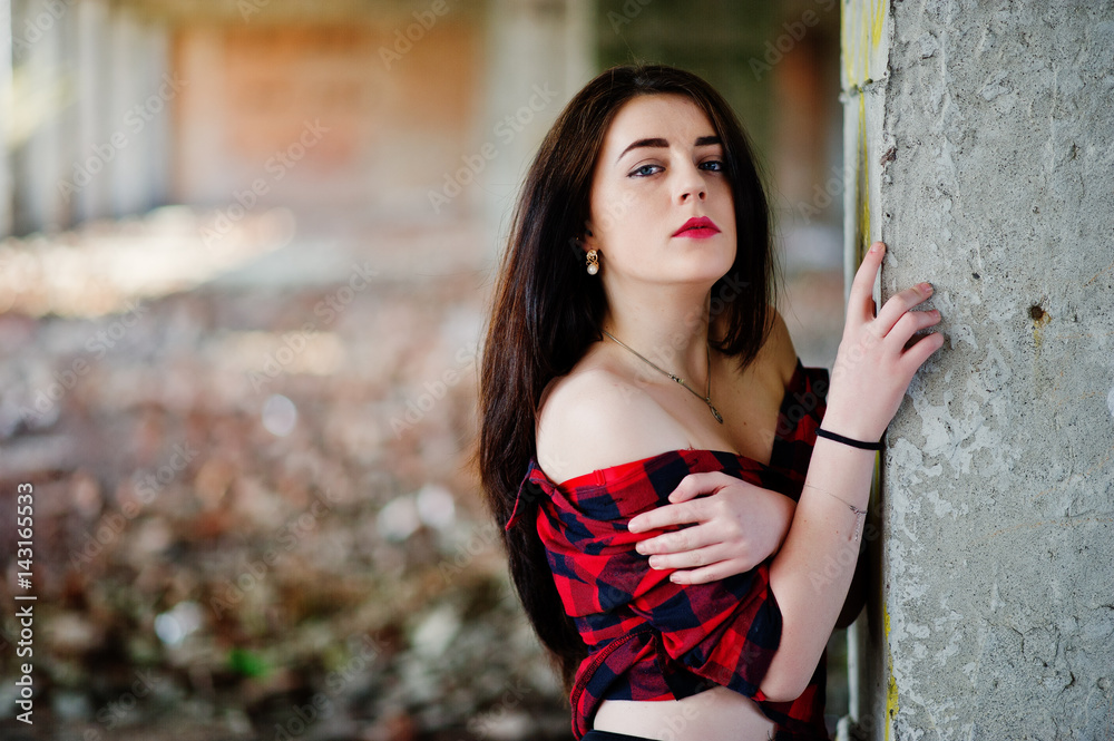 Obraz premium Portrait girl with red lips wearing a red checkered shirt with bare shoulders posed sexy background abadoned place.