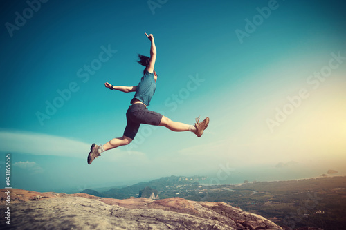 successful woman jumping on rocky mountain peak, freedom, risk, challenge, success concept