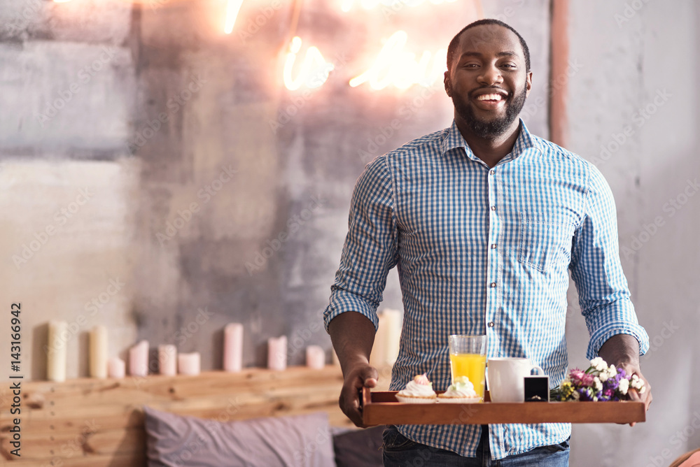 Charismatic African American man holding breakfast tray in the bedroom