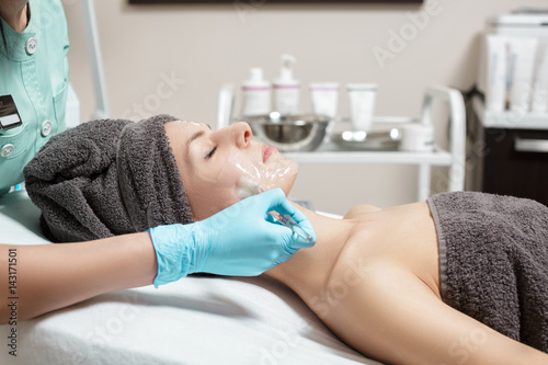 beautician applies face mask with brush to beautiful young woman in Spa salon. cosmetic procedure skin care.