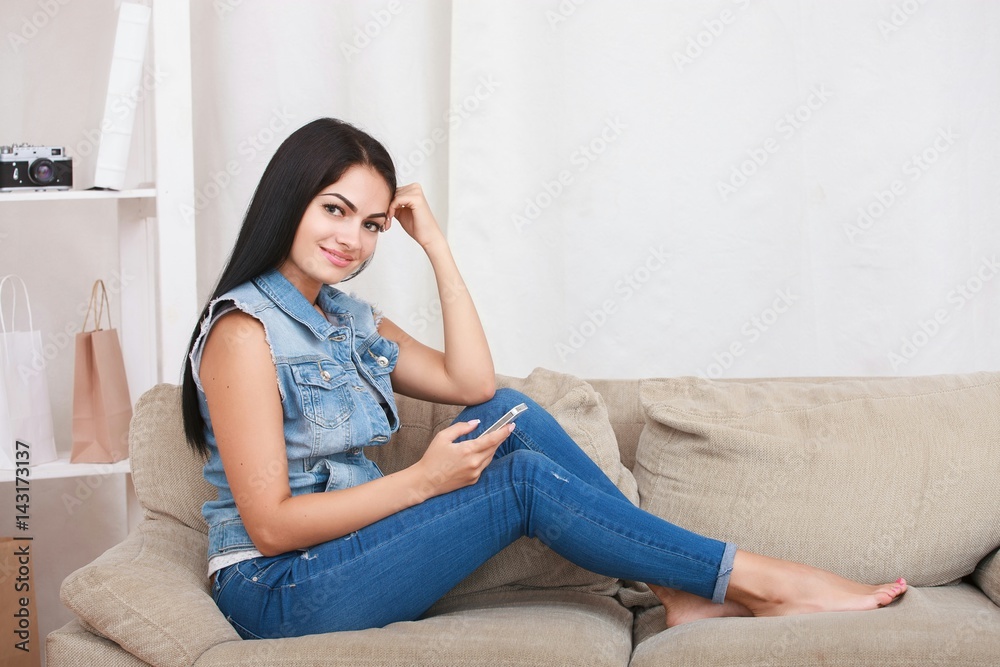 Happy girl reading a message in a smart phone sitting on a couch at home