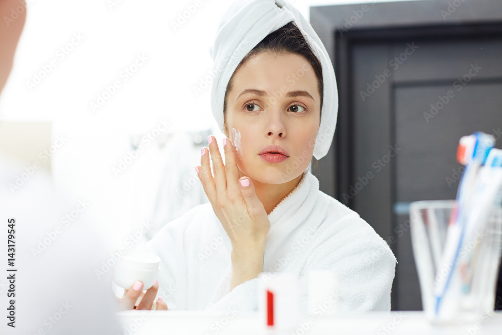 Pretty girl applying moisturizing cream on her face Pretty girl applying moisturizing cream on her face