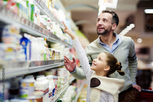 Fotografia Happy girl pointing at pack of youghurt on upper shelf in supermarket