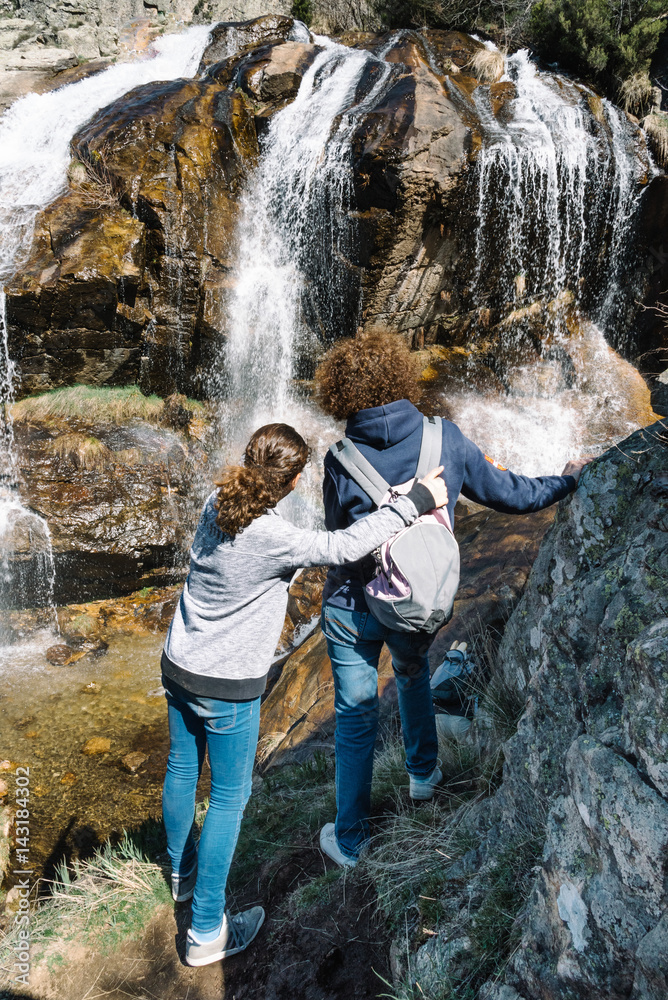 Full Length Portrait Of Mother And Daughter Standing On Rock Against Waterfall At Forest Full Length Portrait Of Mother And Daughter Standing On Rock Against Waterfall At Forest