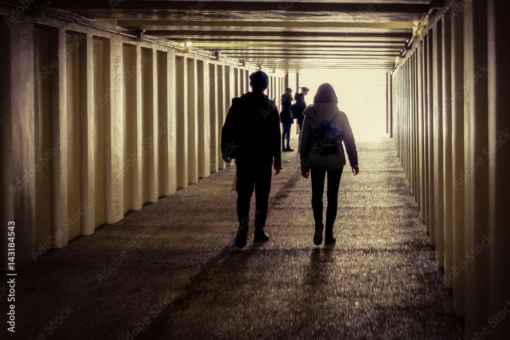A couple of teenagers walks in the underpass with a group of girls staying at the entrance