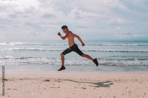Sport - runner running and sprinting on the beach near the ocean. Athlete man during sprint run at great speed. Fitness man wearing compression shorts. Sportsman jump on the beach