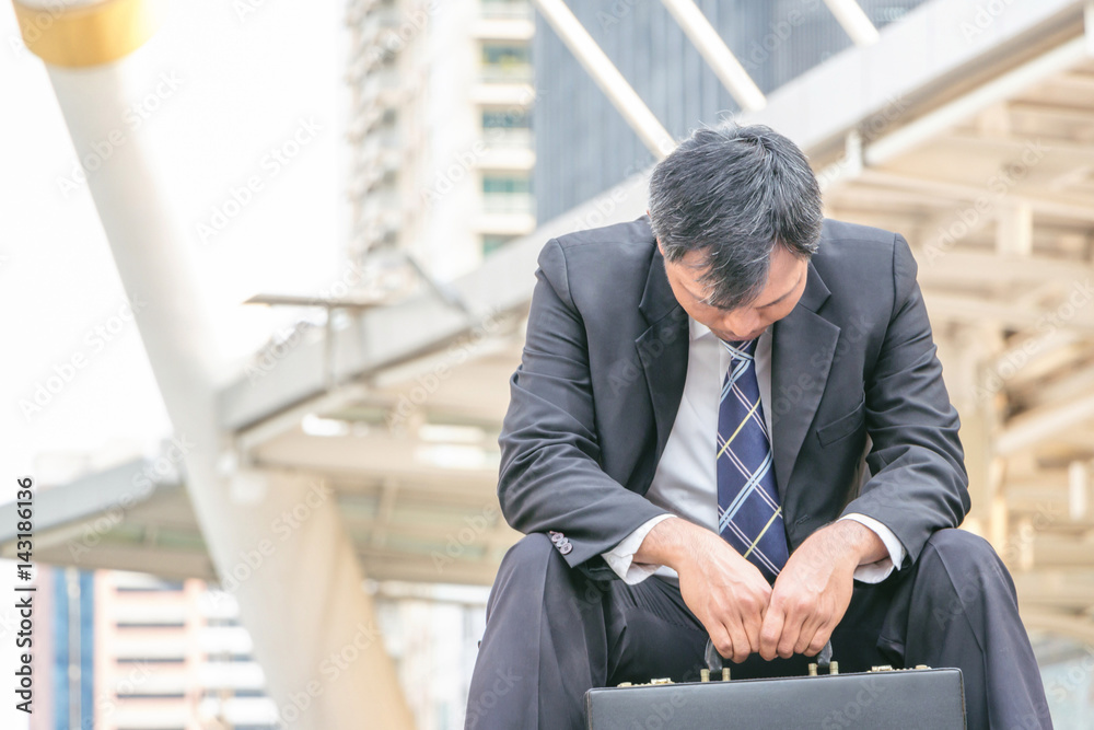 Close up of young business man sitting failed and stressed outside office blurry city background.