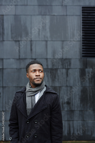 Portrait of handsome African - American business man standing in rainy street against concrete background, looking away