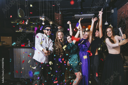 Young cheerful company of friends in the club bar having fun with multi-colored confetti and crackers celebrate