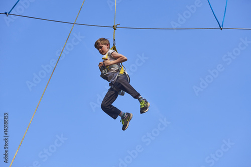 Cute school boy enjoying a sunny day in a climbing adventure activity park. Clear blue sky background. Children summer activities.