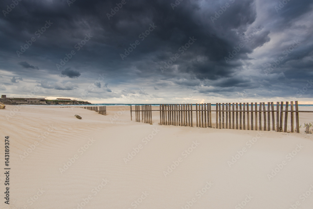 wooden fence on dunes and beach at storm weather