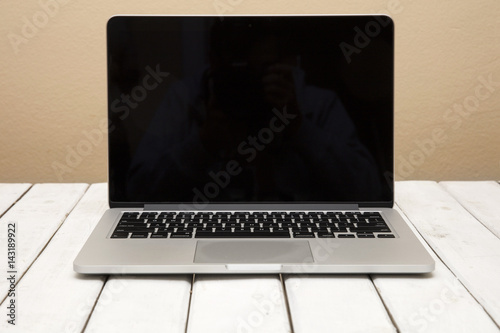 Laptop with black screen on white wooden table by orange background