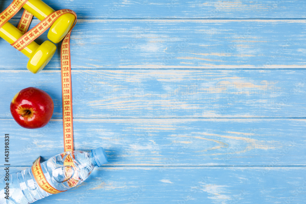 Bottle of water, apple, dumbbells and measure tape on blue wood background. Bottle of water, apple, dumbbells and measure tape on blue wood background.