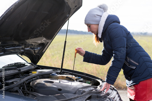 attractive brunette in front of her car broken down car.