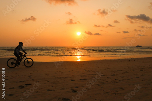 Silhouette of a man rides a bike at sunset. The men Exercise by bike riding on the beach. © jitanong714