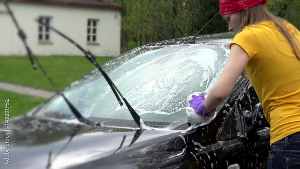 Female cleaning dirt from car with sponge and automobile shampoo.