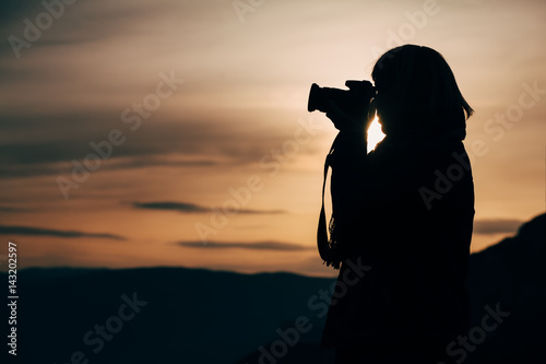 Girl taking photo on mountain peak at sunset