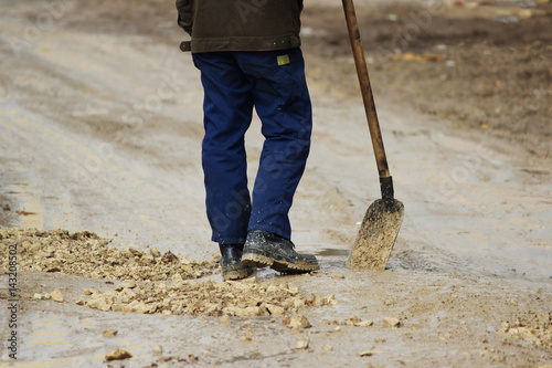Konstfotografi A worker with a shovel strews gravel in pits to level the road