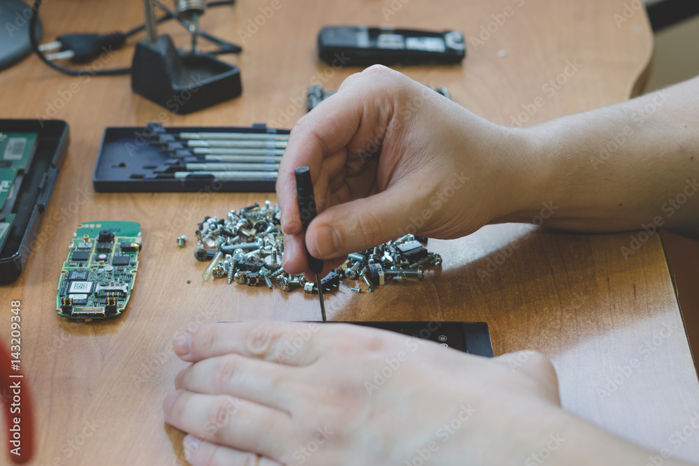 Fototapeta premium repairing broken cellphone mobile by technician. only hands on the desk visible with a lot of screws, screwdrivers and broken phone