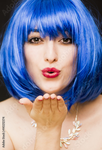 Beauty woman in blue wig and sunglasses  giving a kiss to the air. Portrait isolated on black background