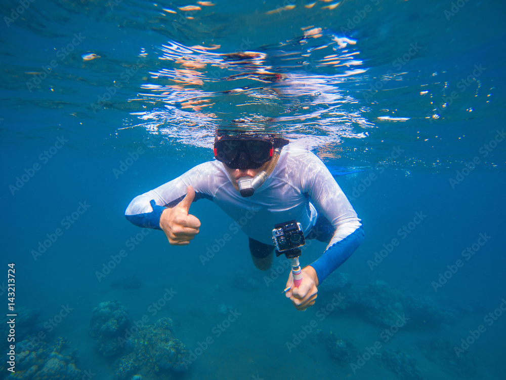 Young sportsman in snorkeling mask shows thumb underwater.
