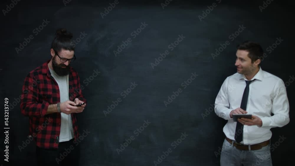 Happy casual businessmen using interactive technology together on chalkboard Happy casual businessmen using interactive technology together on chalkboard