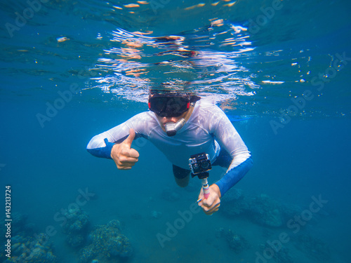 Young sportsman in snorkeling mask shows thumb underwater.