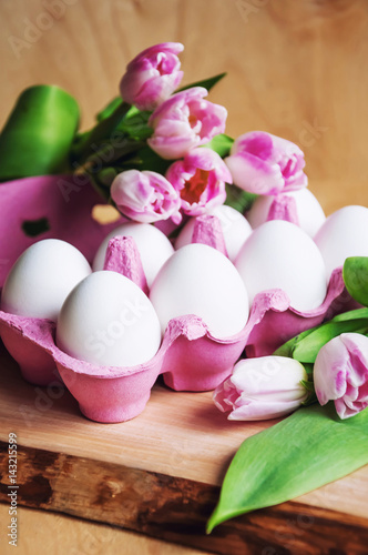 Easter greeting card with eggs in a carton and pink tulips on wooden background, closeup, selective focus