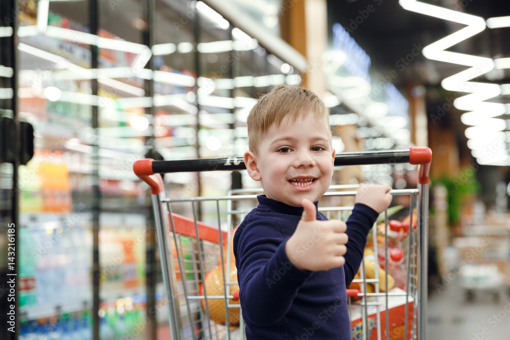 Happy boy near shopping trolley showing thumb up